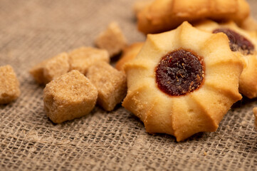 Homemade pastry cookies with jam and pieces of brown cane sugar on a background of homespun fabric with a rough texture, close-up, selective focus.