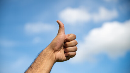 Thumbs up in the blue sky with cotton clouds	