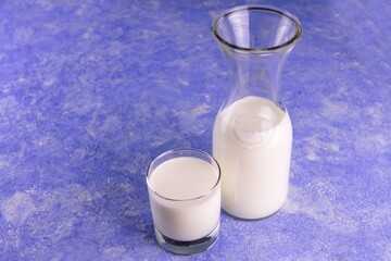 
Milk in a decanter and a glass on a blue background. Copy the request.