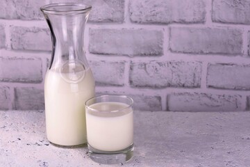 Milk in a decanter and a glass on a white background. Copy the request.