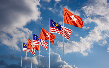 Obraz premium The Malaysian and Hong Kong flags fly together in the wind against the blue sky. The concept of cooperation and competition in economics and politics. Flag of the Malaysia to the left of Hong Kong.