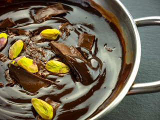 Melted dark chocolate with pistachios. Saucepan with cocoa mousse. Liquid chocolate. Cooking sweets at home. Prepare a dessert. Cacao hot cream. Top view  close up.