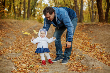 Fototapeta premium Young dad teaches his little daughter to walk in the Park in the fall
