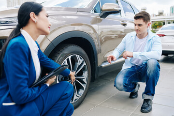 Young man asking saleswoman questions about alloy wheels of car he is going to buy