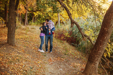 Young parents with a child in their arms walk along the path in the autumn Park