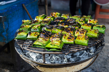 Traditional Thai style food on the grill, marinate fish in banana leaf on the grill at the food market in Thailand