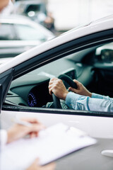 Man sitting in new car in dealership with hands on steering wheel