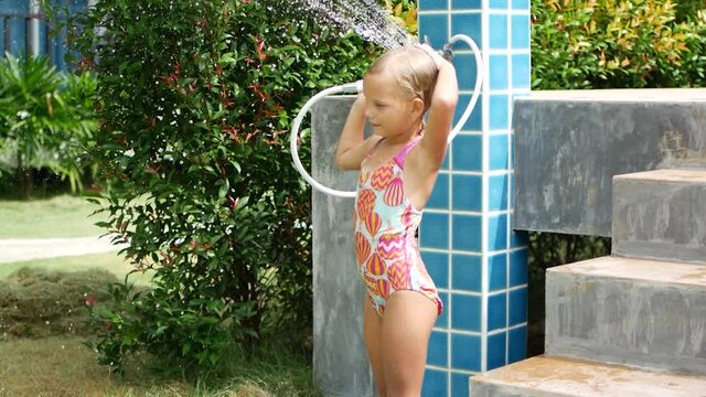 6 year old girl in a swimsuit takes a shower after swimming in the pool, resort in Thailand