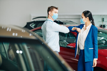Sales manager and customer in medical masks doing elbow bump when greeting each other in car...