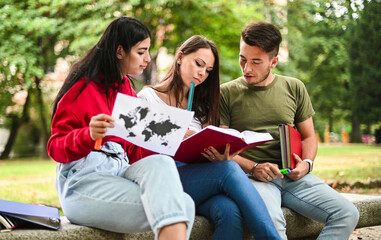 Three students studying together sitting on a bench outdoor