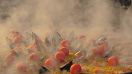 Slow motion: chef cooking paella with shrimp, mussel, rice, tomato, spice, saffron in huge paella pan at summer outdoor food market: close up. Spanish cuisine, seafood, gastronomy, street food concept - Powered by Adobe