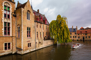 Naklejka premium Bruges, Flanders, Belgium, Europe - October 1, 2019. Medieval ancient houses made of old bricks and the tourist boats that cross the canals in the autumn of Bruges (Brugge)