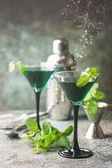 Closeup of green cocktails in martini glasses with mint leaves over gray background