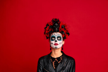Scary young creepy lady calavera. wears artistic make-up for the feast of all the dead. Focused upwards, wears black leather jacket and lace gloves, dressed as skeleton isolated in red.