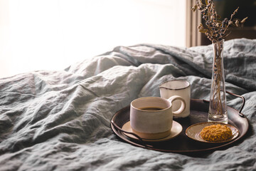 Morning coffee on vintage metal tray in bed with grey sheet and pillows.