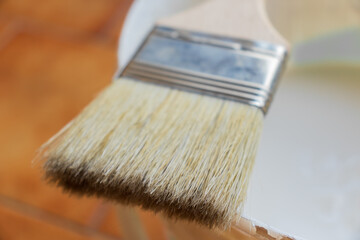 Brush and can of white paint on a terracotta floor