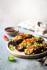 Baked aubergines boats, stuffed with minced meat, tomatoes, corn, garlic and cheese in white plate