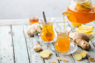 Ginger tea in a glass cup with lemon and mint on light background