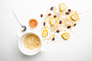 Bowl of oatmeal for porridge with ingredients banana, honey and raisins on white background, healthy breakfast every day, diet food