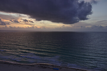 Beautiful storm cloud with orange pink sunset light on horizon above dark ocean