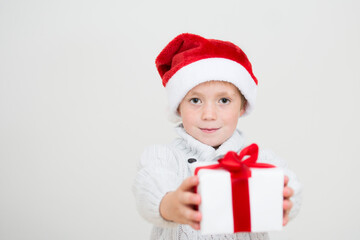 Little boy in red santa hat giving gift box with red ribbon isolated on white background, child giving Christmas present, banner copy space. Isolated on white background.