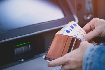 Unrecognizable man putting euro bills withdrawn from the ATM in his pocket wallet