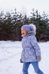 girl in a blue jacket and a fluffy hat plays in the snow in the forest. sincere joy of the child from playing in the fresh air. raising immunity in winter. playing snowballs in the winter forest