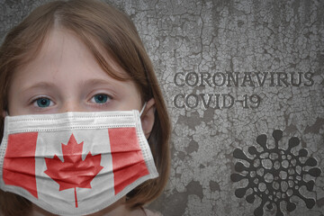Little girl in medical mask with flag of canada stands near the old vintage wall with text coronavirus, covid, and virus picture. Stop virus concept