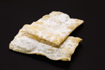 traditional sweet crisp pastry, deep fried for Carnaval, Italian chiacchiere on the black background