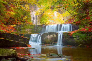 Fototapeta premium Autumn natural landscape - river waterfall in colorful autumn forest with old bridge