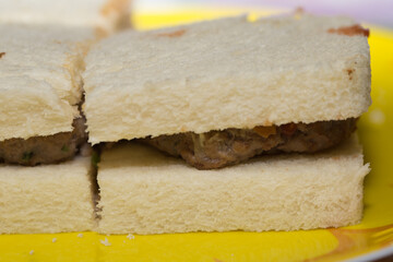 The tramezzino with meatballs with ketchup and mayonnaise on a yellow plate, meatballs in the sandwich