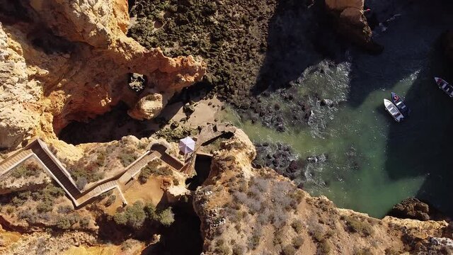 Top down aerial shot of people waiting for boat in Ponta da Piedade with iconic stairs down the cliffs. Low tide Atlantic ocean. Beautiful coastline full of rugged limestone cliffs.