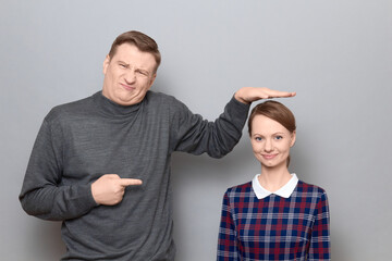 Tall man is showing height of short woman and pointing at her