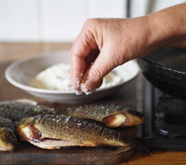 The process of preparing river fish crucian carp for frying in a pan.The hand of an elderly woman salting the fish.