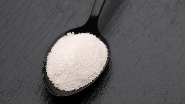 collagen powder in black spoon on black stone, rotating to right.