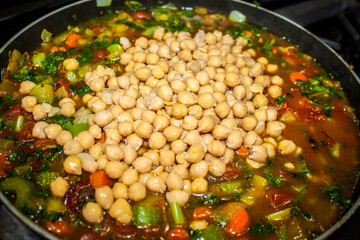 Chickpeas poured into a pot of bubbling soup with vegetables floating around