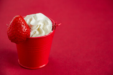 appetizing dessert in a red bucket on a red background, unusual table setting, whipped cream with...