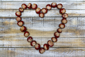 Flat lay chestnut and acorn heart shape on wooden desk. Autumn, wedding top view background