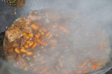 Cooking pilaf in a cauldron on the grill outside in the summer