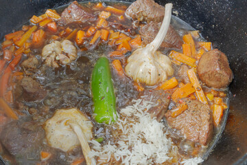 Cooking pilaf in a cauldron on the grill outside in the summer