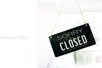 Sorry and Closed sign board through the glass of door in the cafe with clear interior white background and copy space. Cafe closed status during Covid-19 pandemic. Business service and food concept.