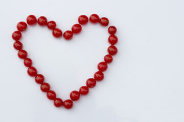 red cherry tomatoes in the shape of a heart on a white background. Flat lay
