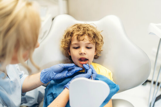 Cute young boy visiting dentist, having his teeth checked by female dentist in dental office.