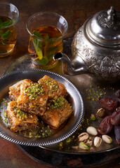 Baklava or baklawa. Ramadan Dessert. Traditional Arabic dessert with pistachios, honey and mint tea on dark surface, selective focus. Ramadan iftar food concept with rosary.