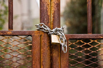 Rusty metal gate of a factory closed with padlock - concept image