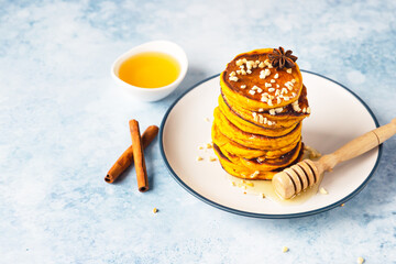 Stack of delicious pumpkin fluffy pancakes with maple syrup or honey and nuts. Healthy breakfast. Autumn food. Blue concrete background.