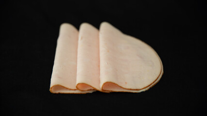 
Trio of poultry ham slice, folded in half, on a black background	