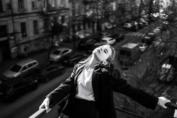Obraz na płótnie Canvas Black and white photo of stylish woman posing on the balcony in the city. Spring autumn fashion concept. Fashionable woman resting on terrace.