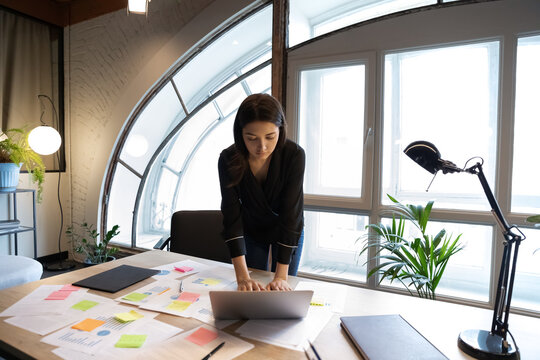 Concentrated young indian ethnicity businesswoman employee using computer application, organizing workflow with creative approach alone in modern office room, current issues or tasks management.