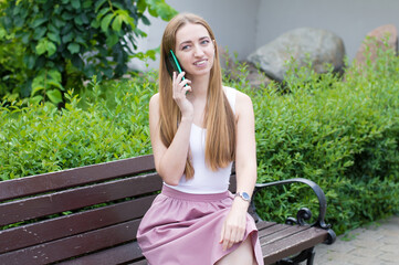 Closeup portrait, young, beathe utiful girl speaking on cell phone, sitting on park bench, isolated...